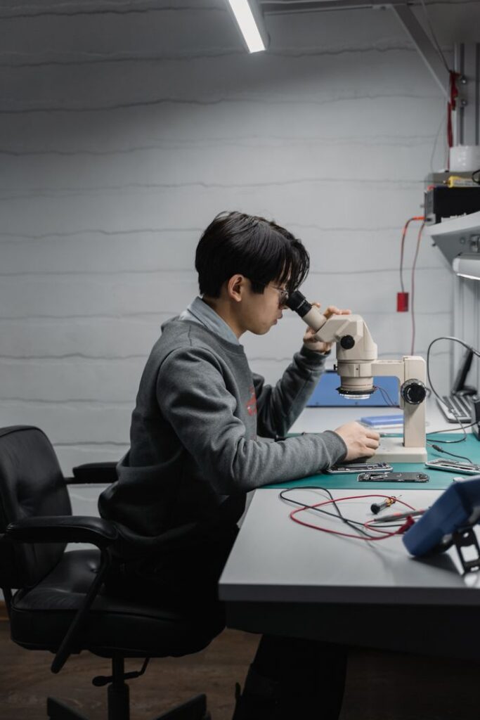 Young engineer focused on electronics work using a microscope in a modern lab workspace.